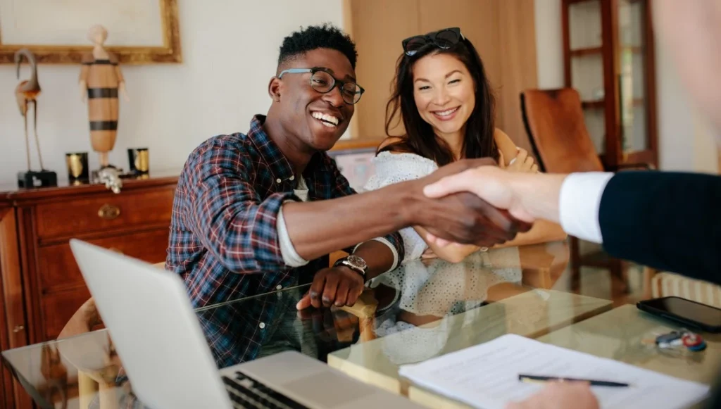 Multicultural couple shaking hand of real estate agent in office, all smiling
