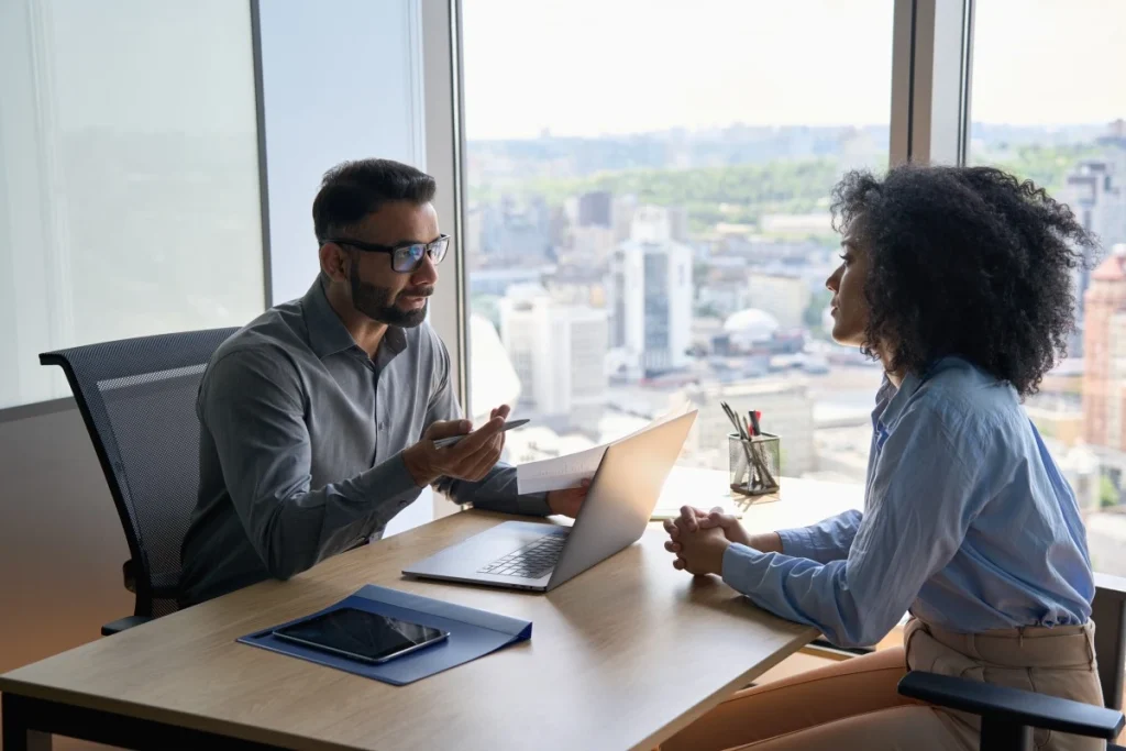 Buyers Agent sitting at desk in front of laptop talking with female client in office about property services