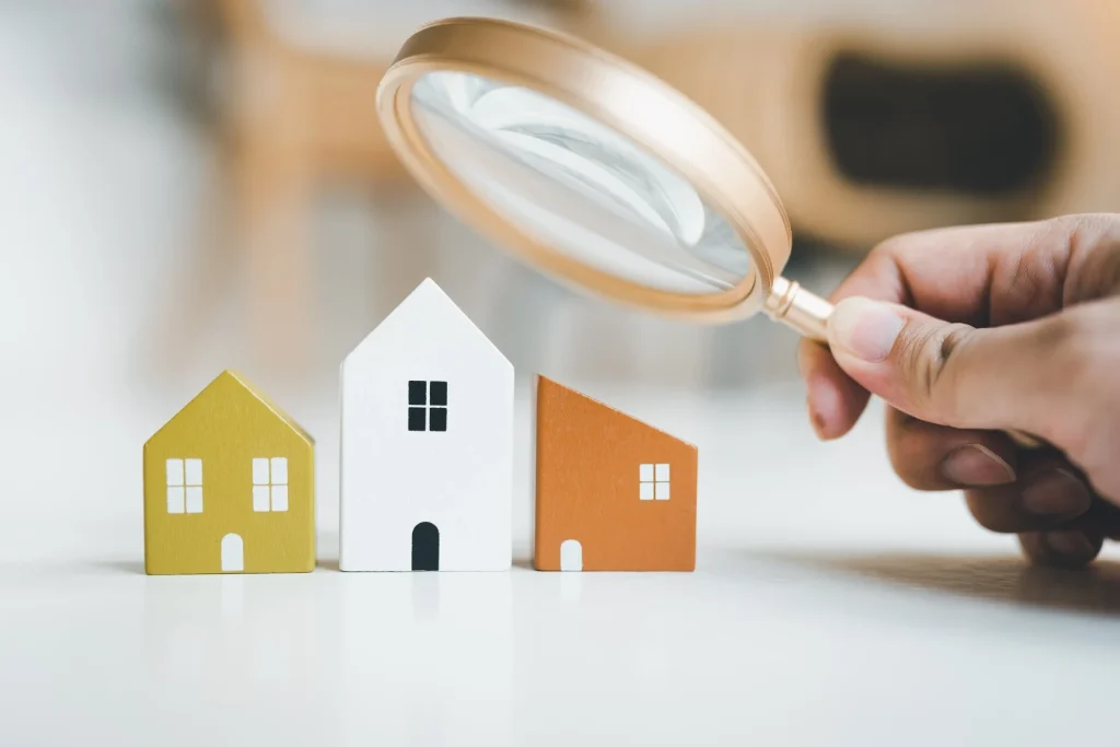 Person holding magnifying glass looking at little toy houses